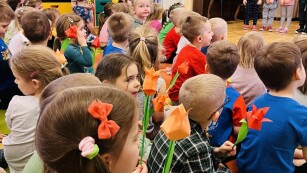 Dzieci z kwiatami w rękach oglądają występ innej grupy