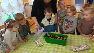Pani Kamila - pomoc nauczyciela podlewa cebulki z dziećmi